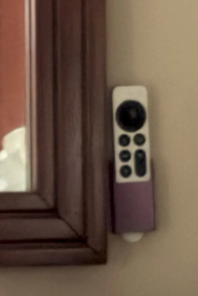 Purple 3D printed wall holder beside a mirror, cradling an Apple TV remote