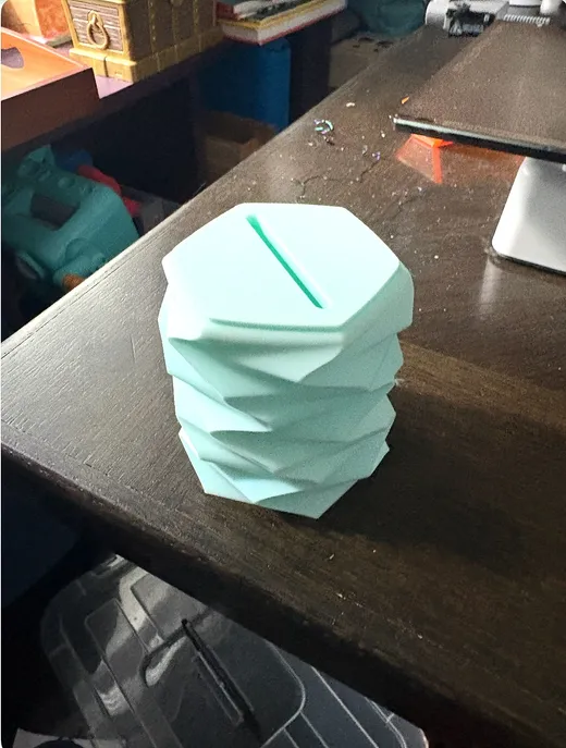Mint green 3D printed piggy bank with a twisted faceted shape and coin slot on top